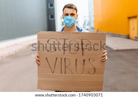 A young man in a medical protective mask holds a cardboard placard reading "Stop the coronavirus" while standing in the city. Quarantine, coronavirus