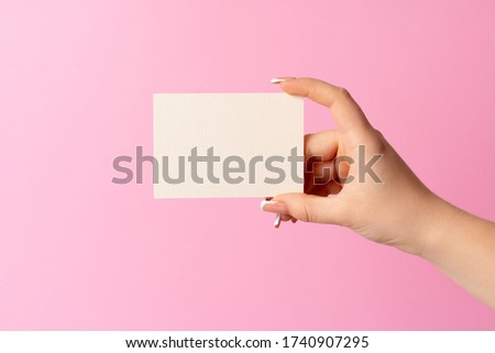 Woman hand showing blank business card on pink background.