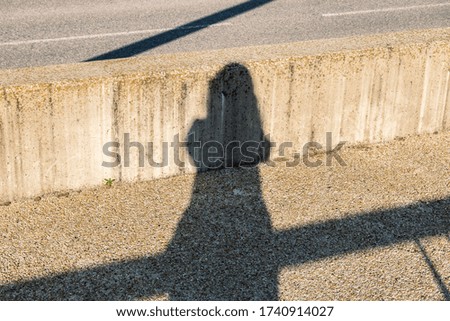 The shadow of a young woman on a concrete sidewalk on a bridge taking a photo on a sunny day