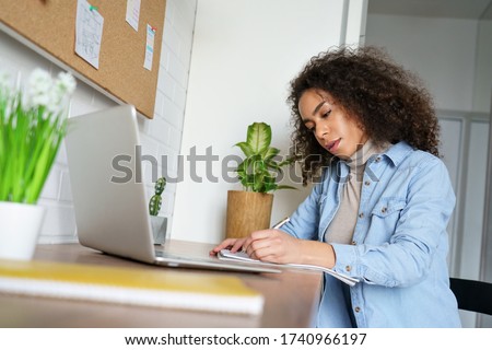 African teen girl, young ethnic woman school student remote worker elearning distance training course work study at home office watching online learning webinar using laptop doing homework notes. Royalty-Free Stock Photo #1740966197