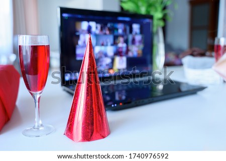 Red holiday hat,glass of juice.Kids virtual birthday party.Celebration of holiday at home on isolation.Online conference,video call in laptop,computer.Animator,cookies.Quarantine,coronavirus covid-19. Royalty-Free Stock Photo #1740976592