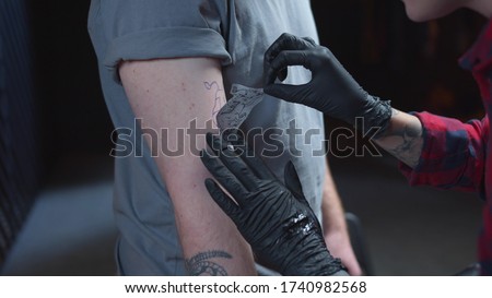 Tattoo master sticks a sketch on a hand of a man