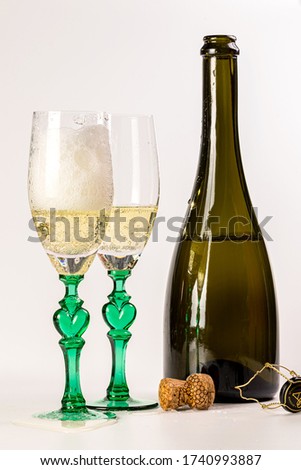 Two glasses of champagne and a bottle on a white background. Creative image with champagne bubbles sparkling in the sun.