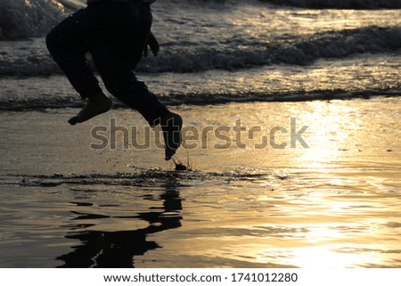 Sunset beach with people / family silhouette playing in the water. Moving ocean water waves in the sun.