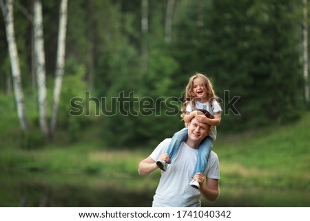 A little daughter is sitting on her daddy's back. They are playing and laughing. Image with selective focus.