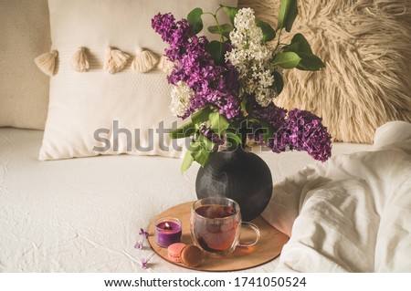 Still life details in home interior of living room. Lilac flowers with hot cup tea. Cozy spring concept.