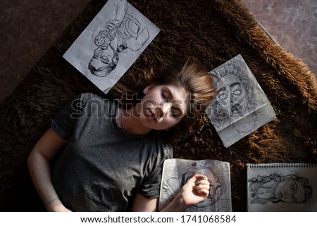 portrait of a girl lying on a sofa around her drawings are scattered, view from above	