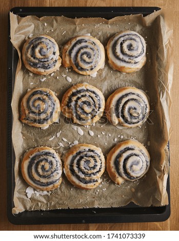 A vertical picture of delicious Poppy snail pastries with a sugar glaze in a tray on a wooden table - perfect background for confectionery shop
