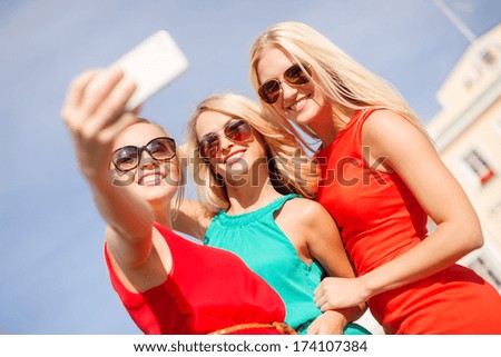 holidays, tourism and modern technology concept - smiling girls taking selfie with smartphone camera in the city
