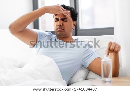 people, bedtime and rest concept - sick indian man lying in bed and dropping medicine pill into glass of water at home
