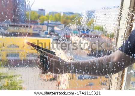 Rubber squeegee in male hand cleans a soaped window. Picture with selective focus. House cleaning, washing windows. Leaves a clear, transparent streak