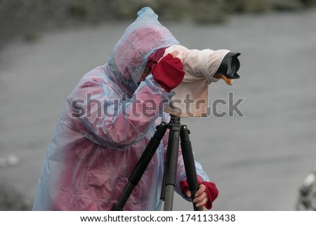 
Photographer wearing a raincoat takes a picture in Jokulsarlon, Iceland with a small iceberg floating in the lake