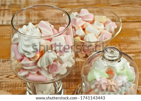 Sweets in a glass on a wooden table. Pink with white soft candies close up.