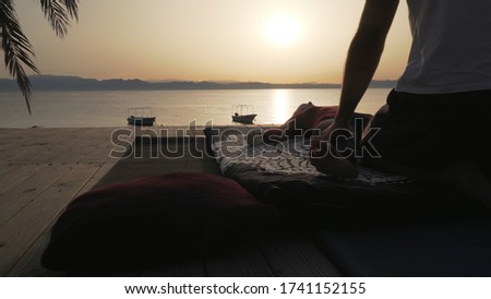 Silhouette person doing massage for a woman at sunset seashore.