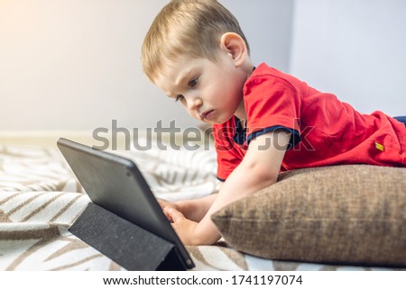 A preschool toddler child watches cartoons on a tablet on the internet while lying on a pillow on the floor. Gadgets and modern entertainment for children.