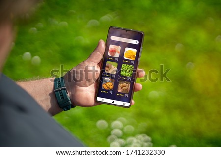 A man's hand is holding a smartphone in his hand. An app is installed on the mobile phone to order food online. The app is fictitious and royalty free.