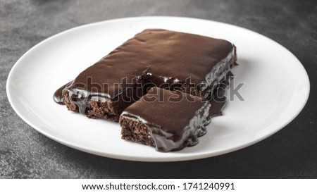 Delicious sliced chocolate cake on a white plate on a grey table background. Tasty homemade cake with dark chocolate glaze topping.
