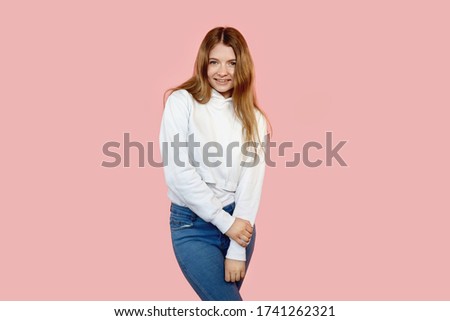 A girl in everyday clothes looks into the camera. Hands are folded together.