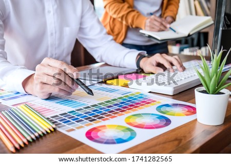 Two colleague creative graphic designer working on color selection and color swatches, drawing on graphics tablet at workplace with work tools and accessories.