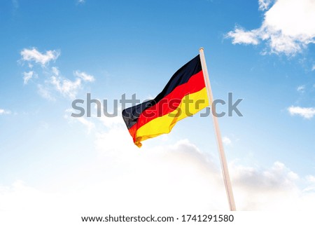 A German flag with black, red and yellow stripes in front of clouds in blue sky