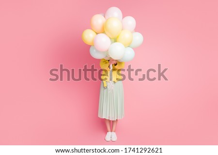 Full length photo of funny playful lady hold hands many air balloons hiding facial expression wear yellow leather jacket green long skirt shoes isolated pastel pink color background