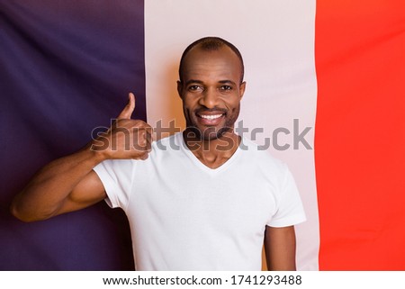 Photo of attractive dark skin guy man standing france national flag good mood raise thumb up wear casual white t-shirt isolated three color flag background