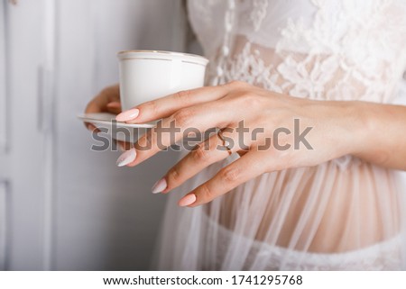 Woman's hand holding a white cup in her hands. Wedding ring on her finger. Focus on it.