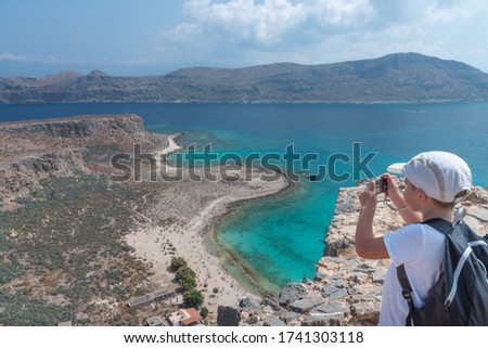 White little boy is taking picture of magical turquoise waters and lagoon on Crete, Greece. Gramvousa fort in Balos lagoon. Family holiday concept.