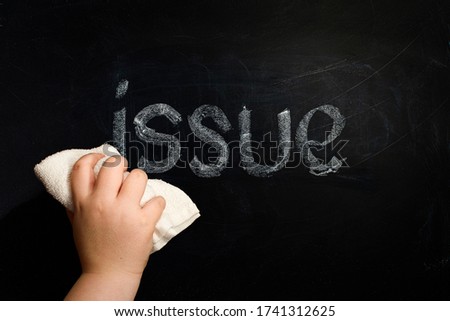 Hand wiping off chalk word issue on chalkboard using rug Royalty-Free Stock Photo #1741312625