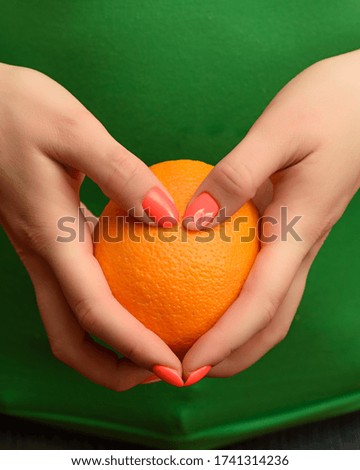 A girl with a beautiful orange manicure is holding a ripe orange in her hands. Close-up photo.