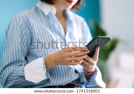 Young woman using mobile phone while working at home with laptop. The girl chatting with friends in social network, shopping online, writing email  using phone. Technology, freelance and work concept.