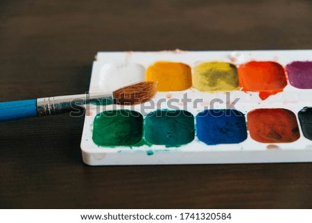 Set of watercolor paints with a brush for painting on a dark wooden background. Copy, empty space for text