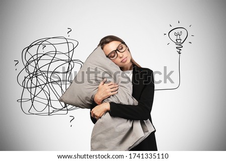Portrait of sleeping young European businesswoman in glasses hugging her pillow near gray wall with creative idea sketch. Concept of healthy sleep and its usefulness for productivity
