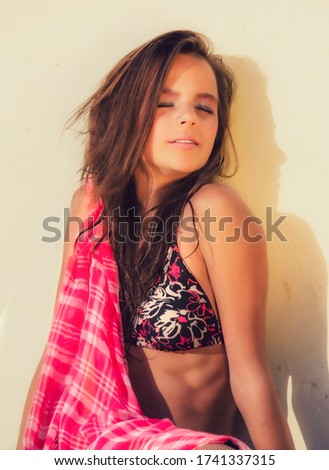 Beautiful young girl in bright bikini swimsuit sitting near wall. Fashionable resort