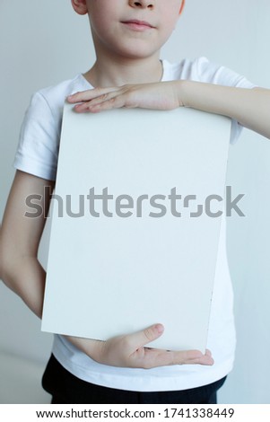 Nice boy dressed in a white T-shirt holds a wooden painted board in his hands. place for advertising. close-up
