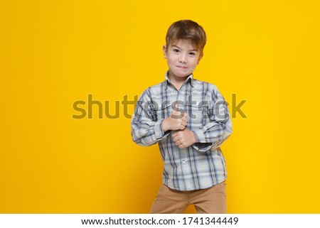 Little cute boy in a checkered shirt shows thumb up, isolated on a yellow background.