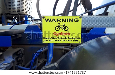 Yellow warning sign for cyclists with bicycle symbol on side of concrete truck. Health & safety legal sign for big truck, Warning Cyclists, Beware when vehicle is turning left do not pass on this side