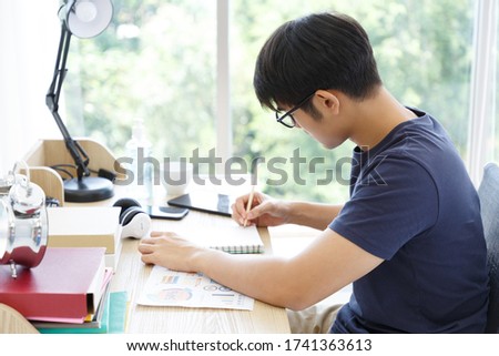 Serious man making note and checking on Paper Chart Report while sitting on Desk in the Bedroom. COPY SPACE. Trading. WORK FROM HOME WFH Concept.