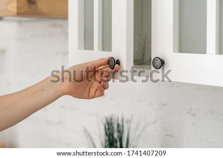 Cropped view of woman hand open door on white cabinets, standing at cozy kitchen in house with modern interior Royalty-Free Stock Photo #1741407209
