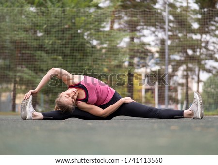 Urban fitness outdoor. Caucasian fit woman doing legs and back stretching on the sports area in summer, selective focus. Outdoor pursuits, workout, healthy lifestyle, yoga, activity, flexibility