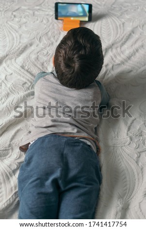 top view of little boy watching webinar on smartphone while lying on bed