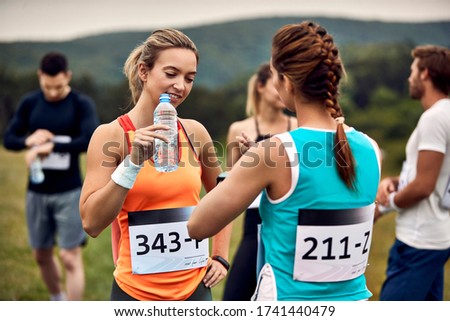 Female runners communicating before marathon race in nature. Focus is on woman with water bottle.  Royalty-Free Stock Photo #1741440479