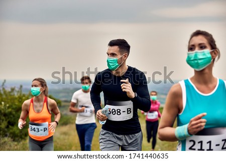 Group of runners wearing protective face masks while participating in a race during virus epidemic. Focus is on man in black shirt. 