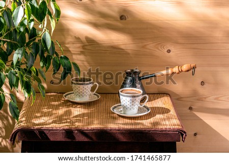 Two cups of coffee and cezve on the table in the patio lit by morning sun.