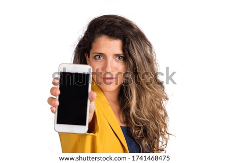 Portrait of young woman showing blank smartphone screen and looking at the camera over white background.