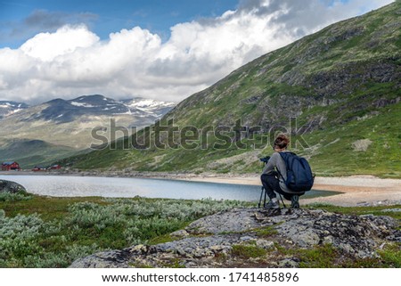 Young woman traveler professional photographer takes a picture of the landscape on the camera on a tripod, Norway, beautiful northern nature