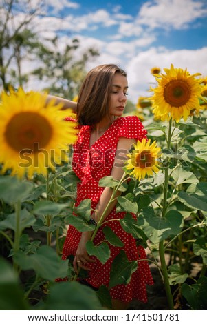 young beautiful caucasian girl in red dress in white dots stay in sunflower field