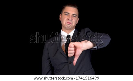 Young businessman shows dislike on hand. Man in a black suit on a black background