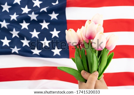 US American flag with hand holding tulip flower on white background. For USA Memorial day, Presidents day, Veterans day, Labor day, Independence or 4th of July celebration. Copy space for text.