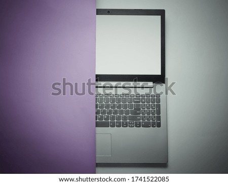 Half of laptop hidden behind purple paper sheet. Minimalism concept. Top view